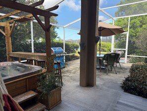 Eine überdachte Terrasse im Freien mit Whirlpool, Holzmöbeln, Grill und Tisch mit Stühlen.