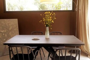 Ein Esstisch mit vier Stühlen, eine Vase mit gelben Blumen und ein Fenster mit Vorhängen.
