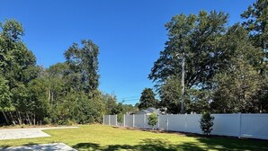 Ein Garten mit Terrasse, weißem Zaun und Bäumen.