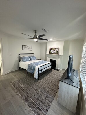 Ein Schlafzimmer mit Bett, Deckenventilator, Kamin und Fernseher.