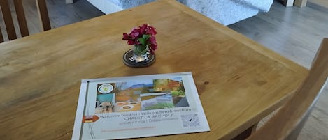 Ein Zimmer mit zwei Betten, einem Holztisch mit einem Begrüßungsbuch und einer kleinen Vase mit Blumen.