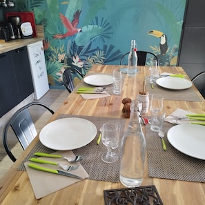 A dining table set with plates, cutlery, and glasses, with a decorative bottle and a bird illustration on the wall behind. - Guest House 'Chambre Bachole' with Mountain View, Shared Pool and Wi-Fi (Charancieu)