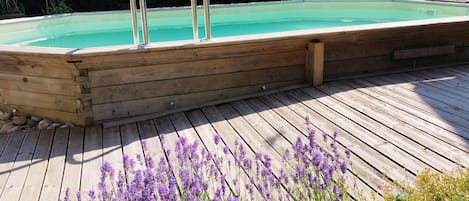 Una terraza de madera con piscina, escaleras de metal y flores moradas.