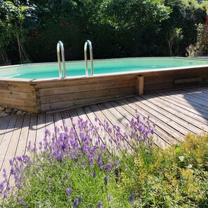 Una terrassa de fusta amb una piscina, escales metàl·liques i flors morades.