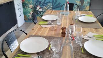 Een gedekte eettafel met borden, bestek en glazen, met een decoratieve fles en een vogelillustratie aan de muur achter de tafel.