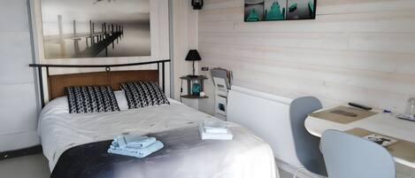 A bedroom with a bed, bedside table, lamp, and a desk with a chair.