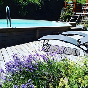 Una terrassa de fusta amb piscina, gandules i flors morades.