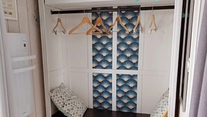 A room with a white wardrobe featuring a blue and white fan pattern, a small table with a patterned cushion, and a hanging clothes rack. - Bed and Breakfast 'Chambre Paladru' with Mountain View, Shared Pool and Wi-Fi (Charancieu)
