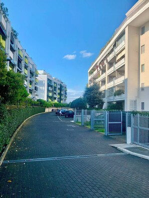 A residential street with modern apartment buildings, a paved road, and a gated entrance. - New Apartment in Eur Mezzocammino + Private Parking Space  (Roma)
