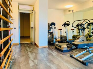 A home gym with exercise equipment, a wooden rack, and a hallway leading to another room. - New Apartment in Eur Mezzocammino + Private Parking Space  (Roma)