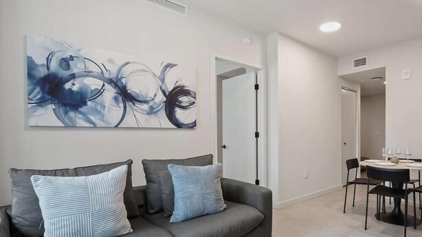 Ein modernes Wohnzimmer mit einem grauen Sofa, zwei Kissen und einem großen abstrakten Gemälde an der Wand.