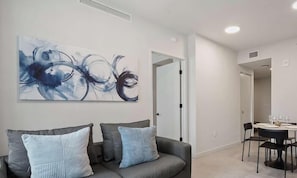 A modern living room with a grey sofa, two pillows, and a large abstract painting on the wall. - Modern Balcony Condo Near Kaseya and Museums (Miami)