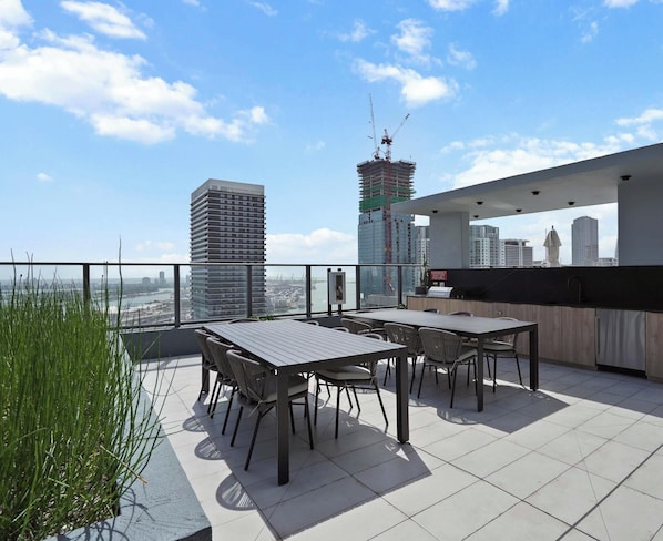 A rooftop terrace with a view of a city skyline, featuring a high-rise building and a construction crane. - Modern Balcony Condo Near Kaseya and Museums (Miami)