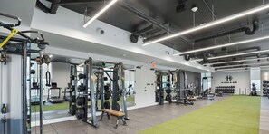 Ein modernes Fitnessstudio mit Gewichthebern, einem grünen Rasenbereich und einem gut sichtbaren Ausgangsschild.