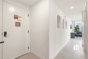 A modern hallway with a door, a welcome sign, an evacuation plan, and a view into a living area with a sofa and a plant. - Skyline Apartment | Balcony, Pool & Near Museums (Miami)