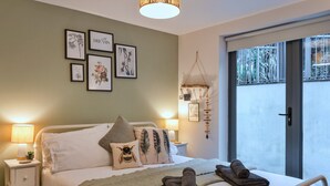 Quarto com cama, almofadas, mesa de cabeceira com abajur, decoração na parede e vista pela janela.