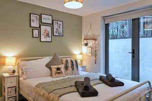 Ein Schlafzimmer mit Bett, Kissen, einem Nachttisch mit Lampe, einer Wanddekoration und Blick durch ein Fenster.