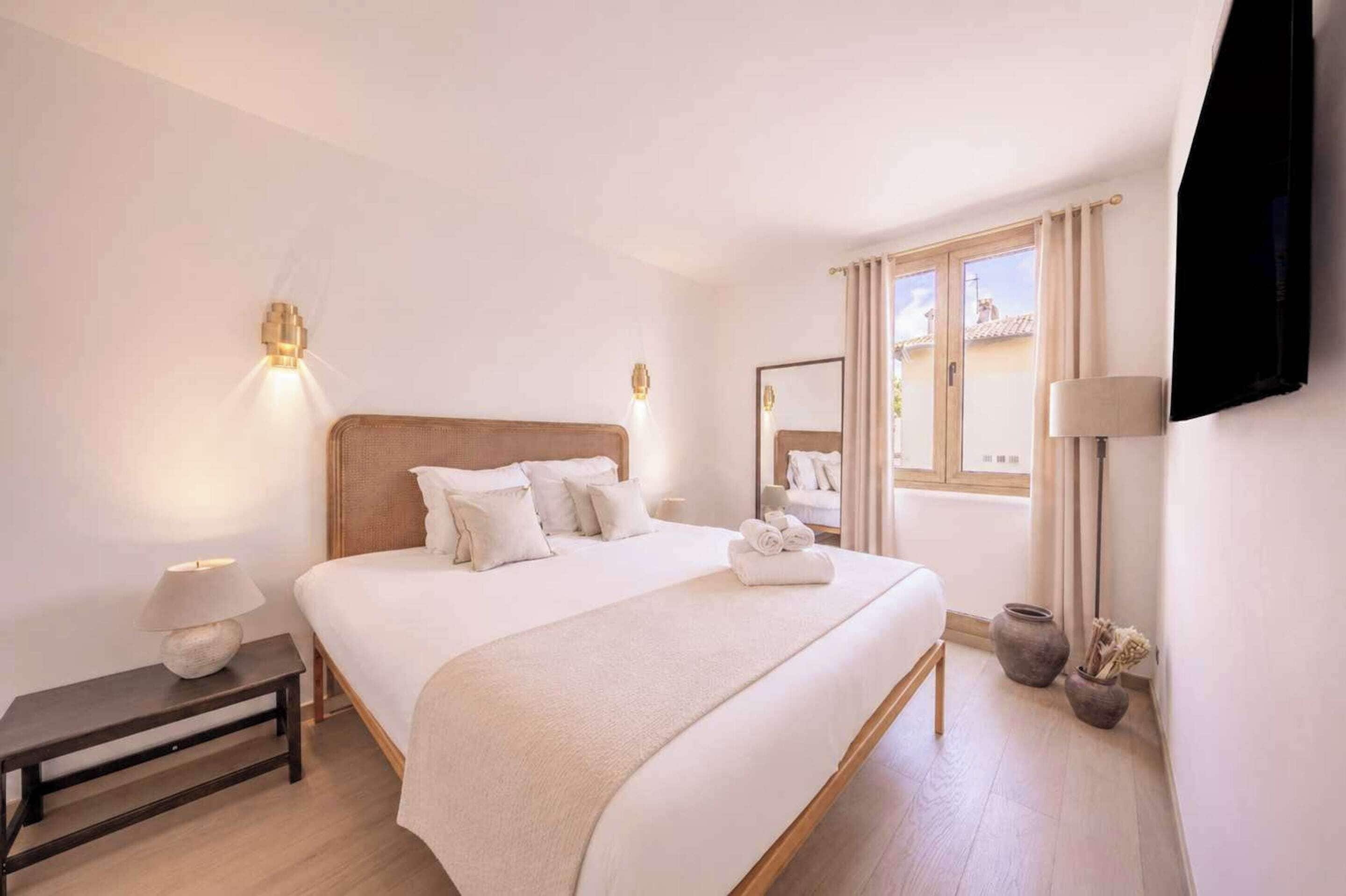 Habitación de hotel con una cama grande, lámparas de noche, mesita de noche, una ventana con cortinas y un televisor de pantalla plana montado en la pared.
