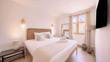 Habitación de hotel con una cama grande, lámparas de noche, mesita de noche, una ventana con cortinas y un televisor de pantalla plana montado en la pared.