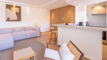 A modern living room with a sofa, a small table, and a chair. There is a kitchen area with a counter and a stove.
