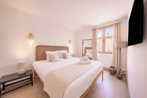 Habitación de hotel con una cama grande, lámparas de noche, una mesita de noche, un televisor de pantalla plana en la pared y una ventana con cortinas.
