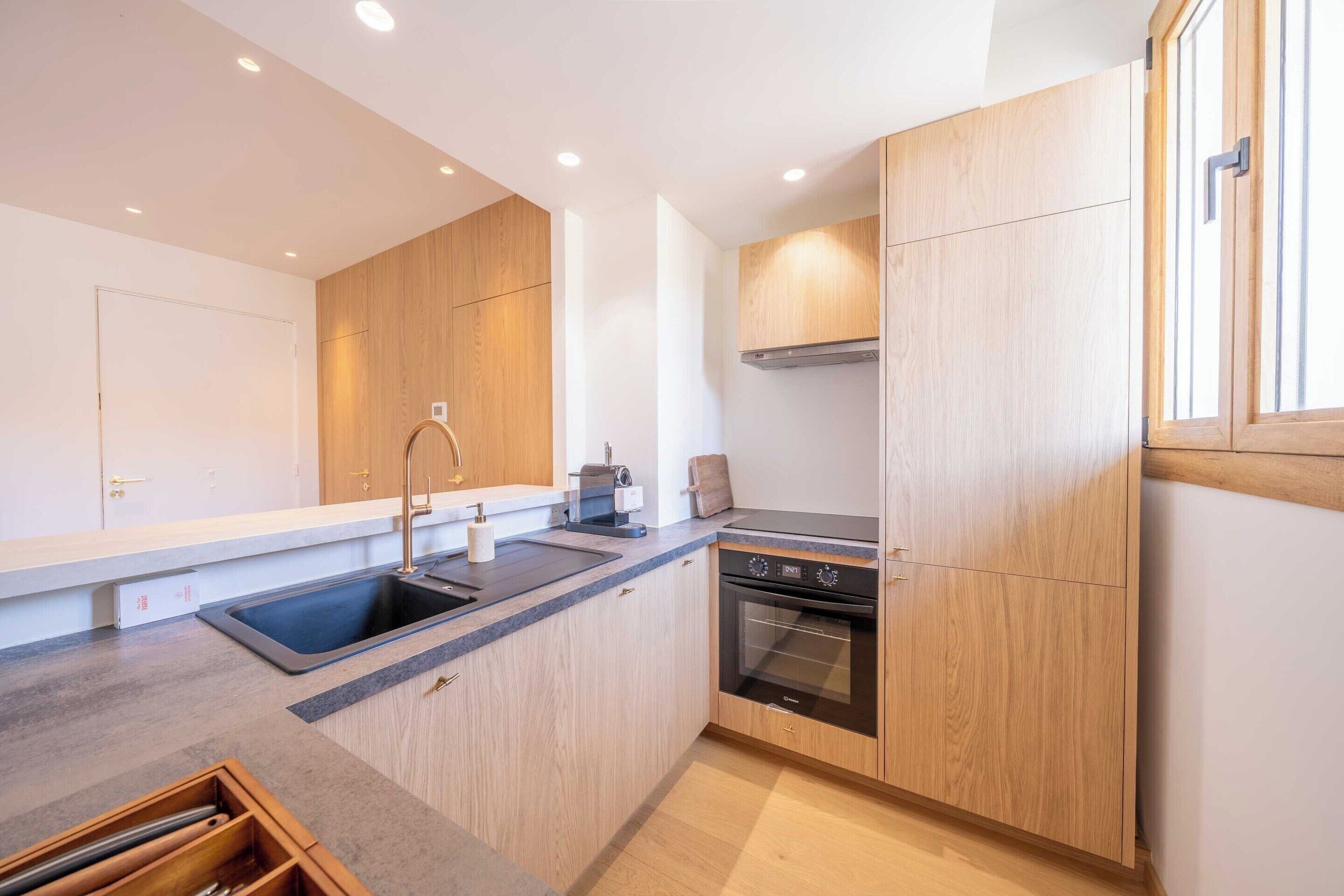 Una cocina moderna con armarios de madera, un lavamanos de acero inoxidable, horno empotrado y máquina de café.