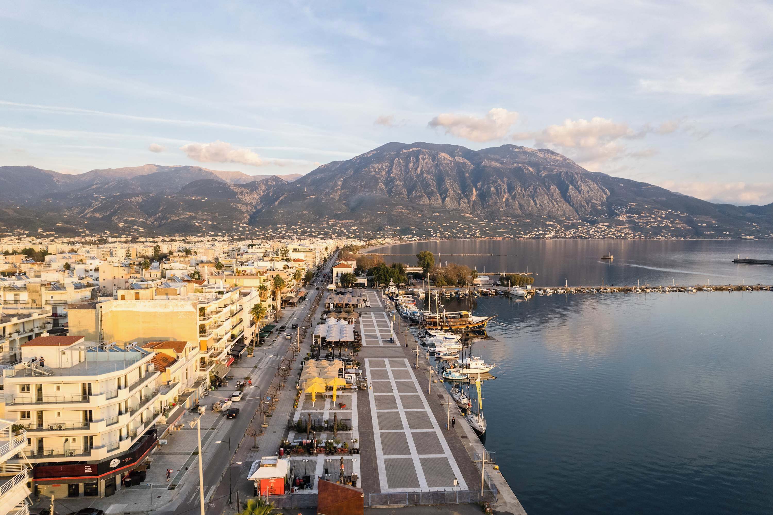 A coastal cityscape with a marina, buildings, and mountains in the background.