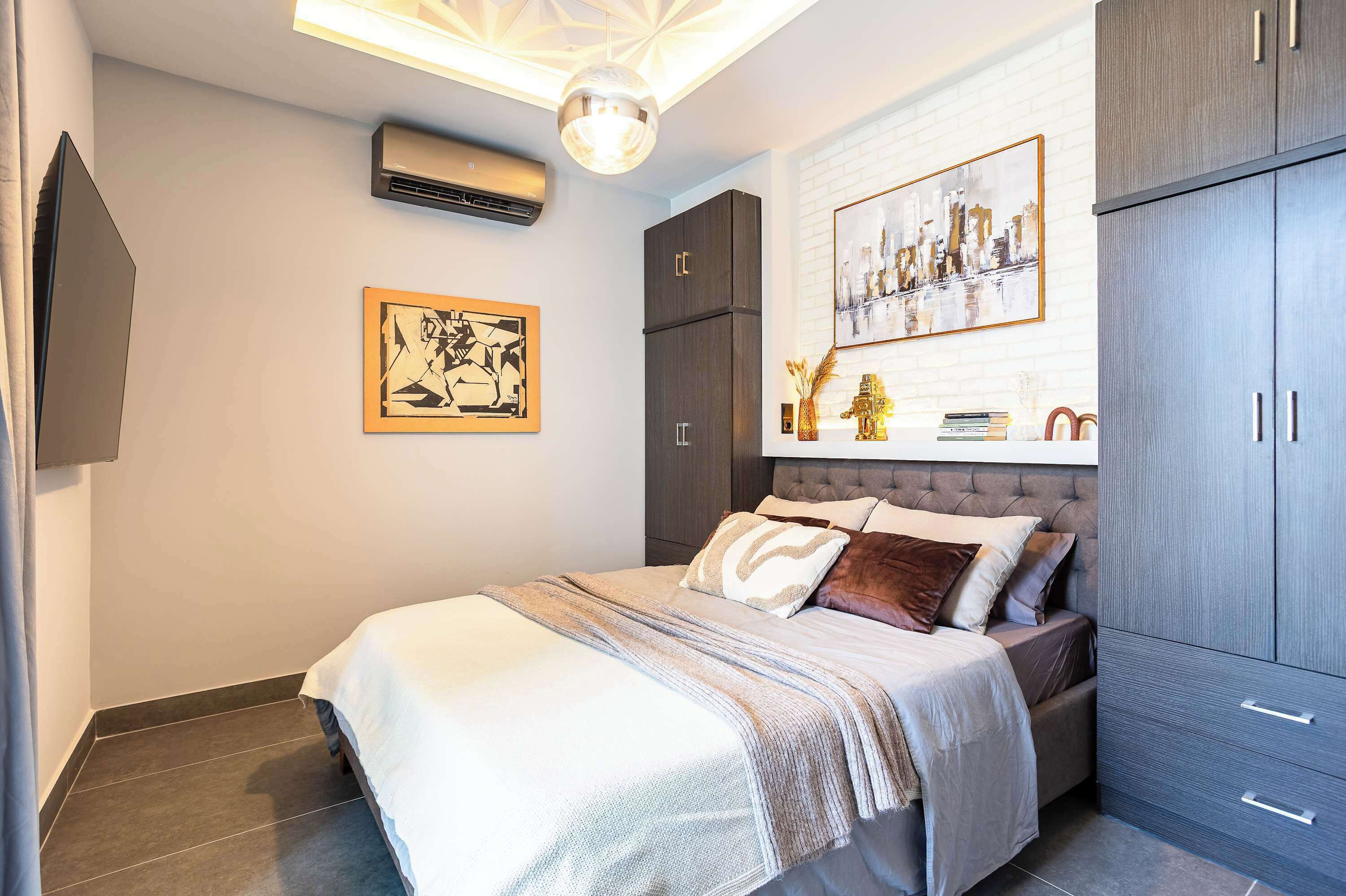 A bedroom with a bed, a wardrobe, a painting, and an air conditioning unit.