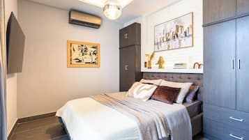 A bedroom with a bed, a wardrobe, a painting, and an air conditioning unit.