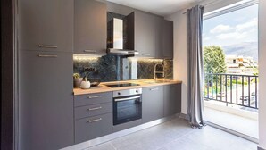 Una cocina moderna con gabinetes grises, un horno negro y un ventanal con vistas a edificios y árboles.