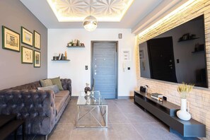 A modern living room with a sofa, coffee table, and a flat-screen TV mounted on a brick wall. - Socrates Suite C3 - Open City Views in Kalamata (Kalamata)
