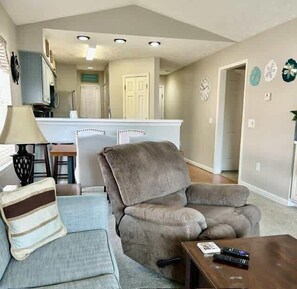 A living room with a sofa, a coffee table, and a lamp. There is a kitchen area in the background with a refrigerator and a microwave. - Cozy Coastal Retreat With Scenic Waterway Views 16I (Myrtle Beach)