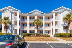 A multi-story hotel with balconies, a parking lot, and palm trees. - Cozy Coastal Retreat With Scenic Waterway Views 16I (Myrtle Beach)