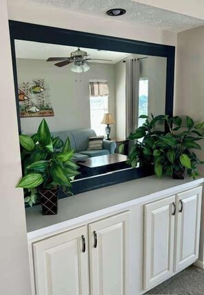 A white cabinet with a large mirror above it, reflecting a room with a ceiling fan, a sofa, and a lamp. - Cozy Coastal Retreat With Scenic Waterway Views 16I (Myrtle Beach)