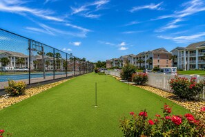 A golf course with a clear sky, a fence, and residential buildings in the background. - Cozy Coastal Retreat With Scenic Waterway Views 16I (Myrtle Beach)