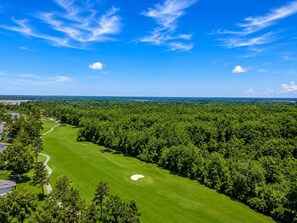 A golf course with a clear sky, surrounded by dense trees and a distant view of a town. - Cozy Coastal Retreat With Scenic Waterway Views 16I (Myrtle Beach)