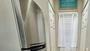 Ein schmaler Flur mit einem Edelstahlkühlschrank, Holzboden und einem Schild über einer Tür.