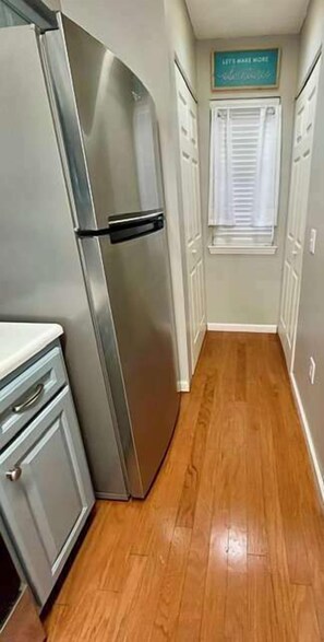 A narrow hallway with a stainless steel refrigerator, wooden flooring, and a sign above a door. - Cozy Coastal Retreat With Scenic Waterway Views 16I (Myrtle Beach)