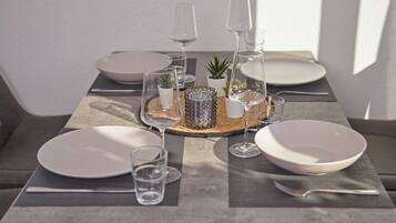 Una mesa de comedor dispuesta con platos blancos, vasos transparentes y una pequeña planta en maceta.