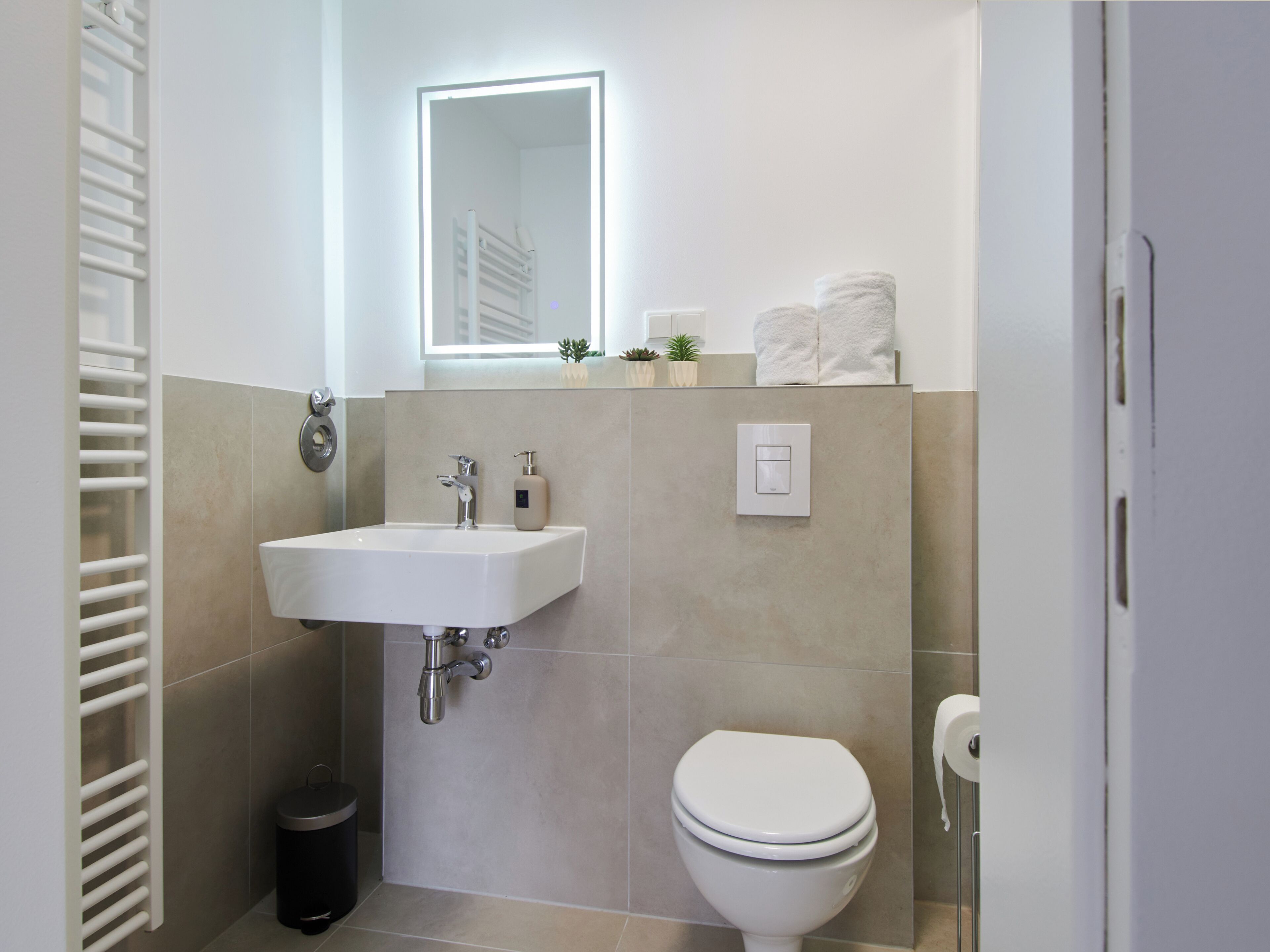 Un baño moderno con un lavamanos blanco, un inodoro y un espejo sobre el lavamanos.