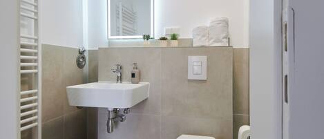 Un baño moderno con un lavamanos blanco, un inodoro y un espejo sobre el lavamanos.