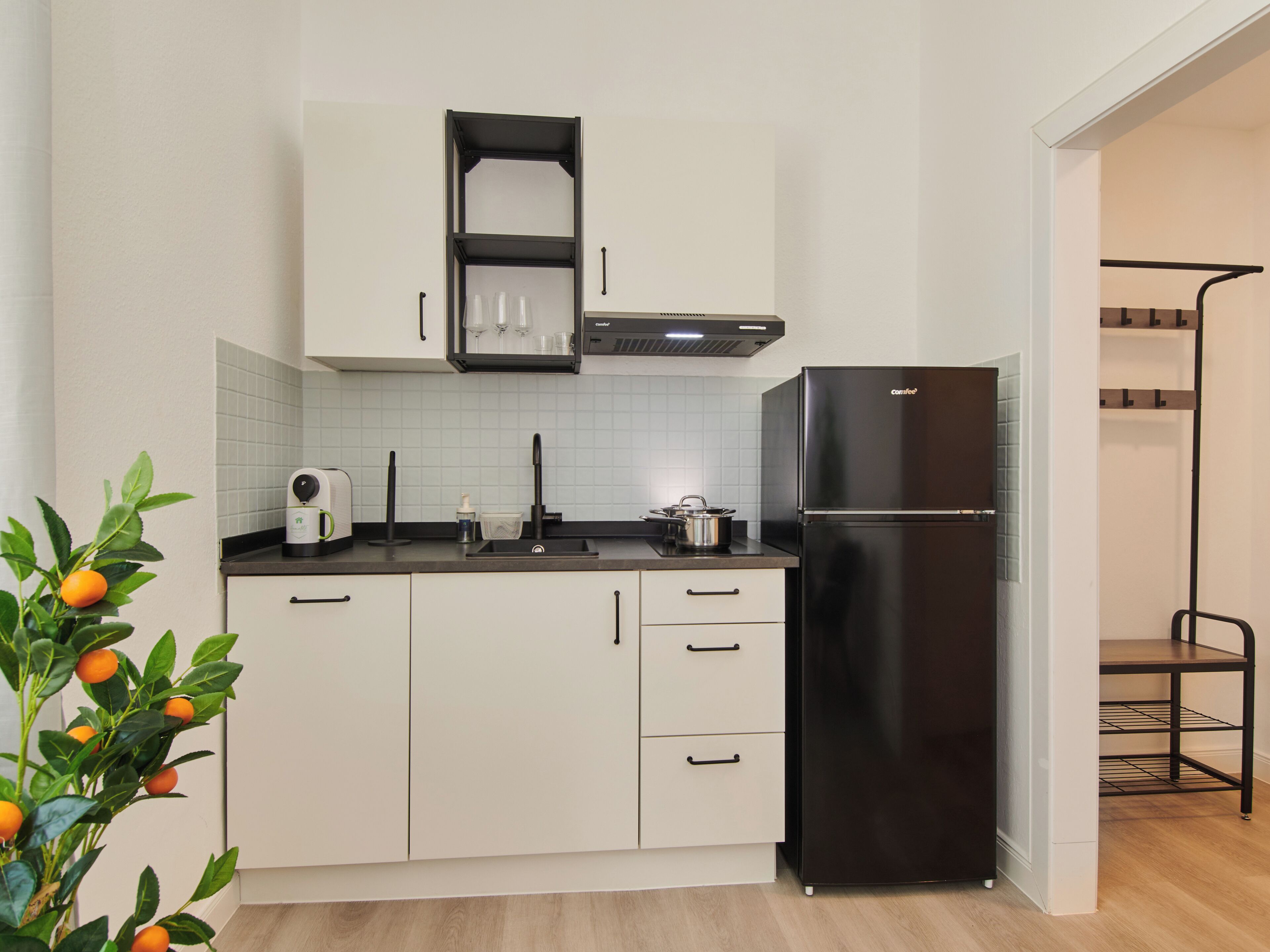 A modern kitchen with white cabinets, a black refrigerator, and a countertop with a coffee maker and a kettle.