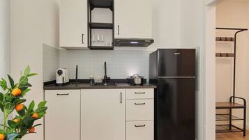 A modern kitchen with white cabinets, a black refrigerator, and a countertop with a coffee maker and a kettle.