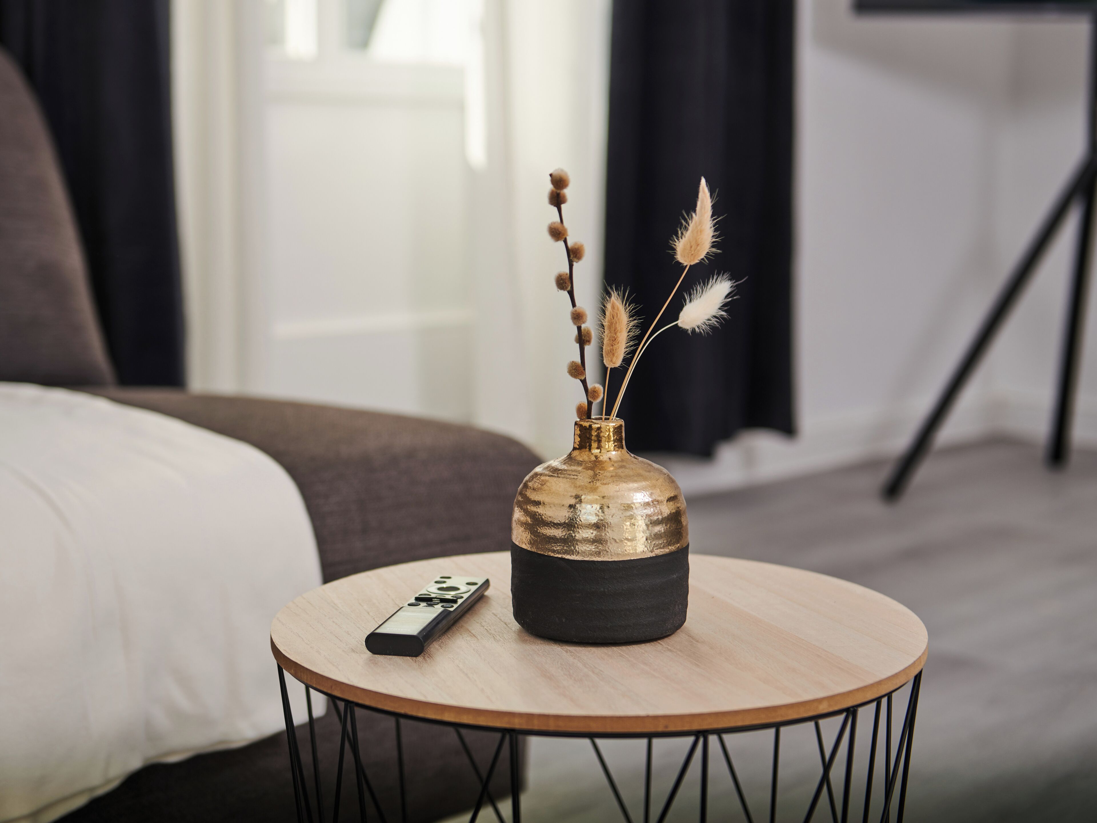 A round table with a remote control and a vase with dried plants.