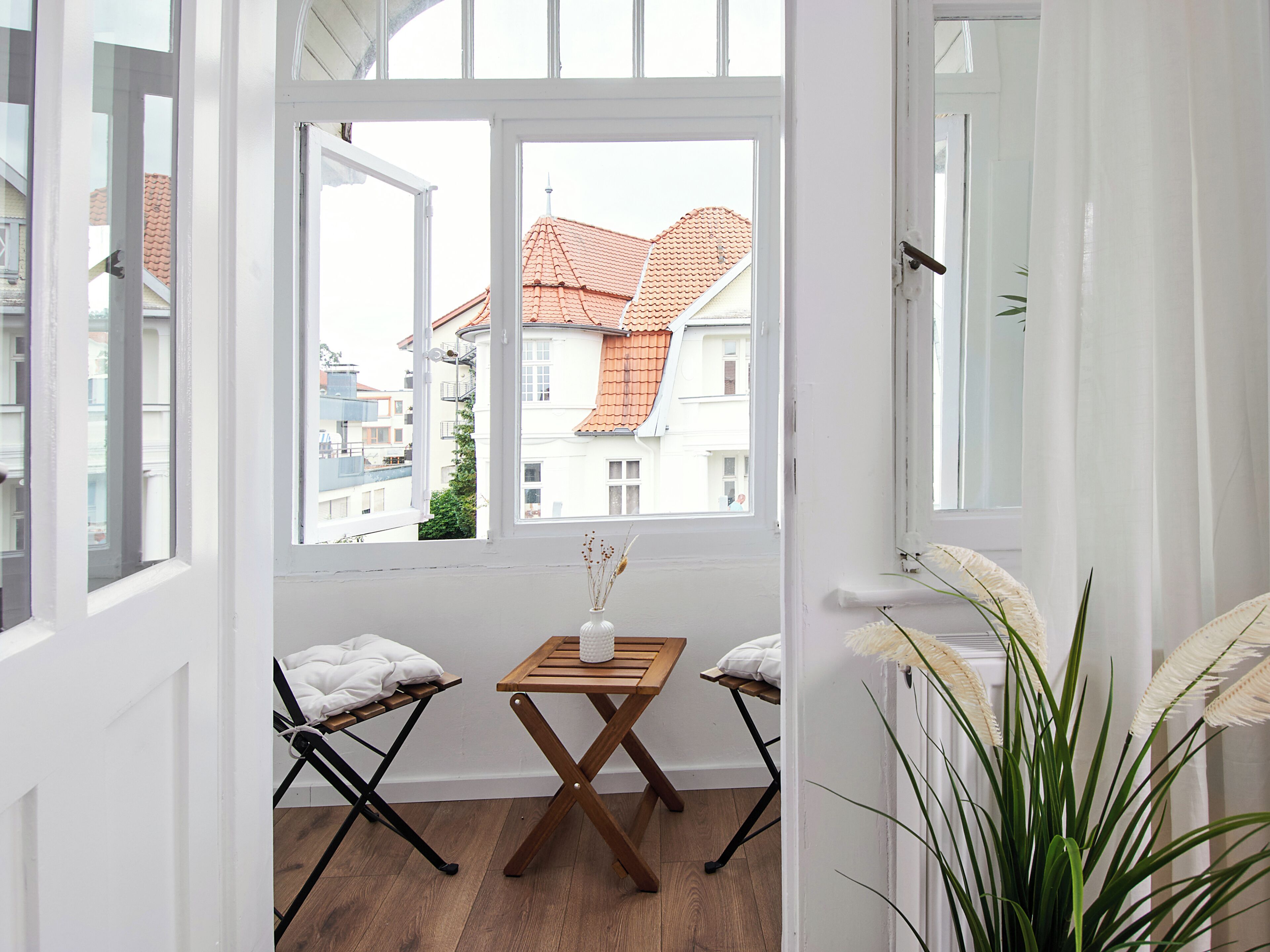 Ein Zimmer mit Blick auf Gebäude durch ein großes Fenster, ein kleiner Holztisch mit einer Vase und zwei Stühle mit Kissen.