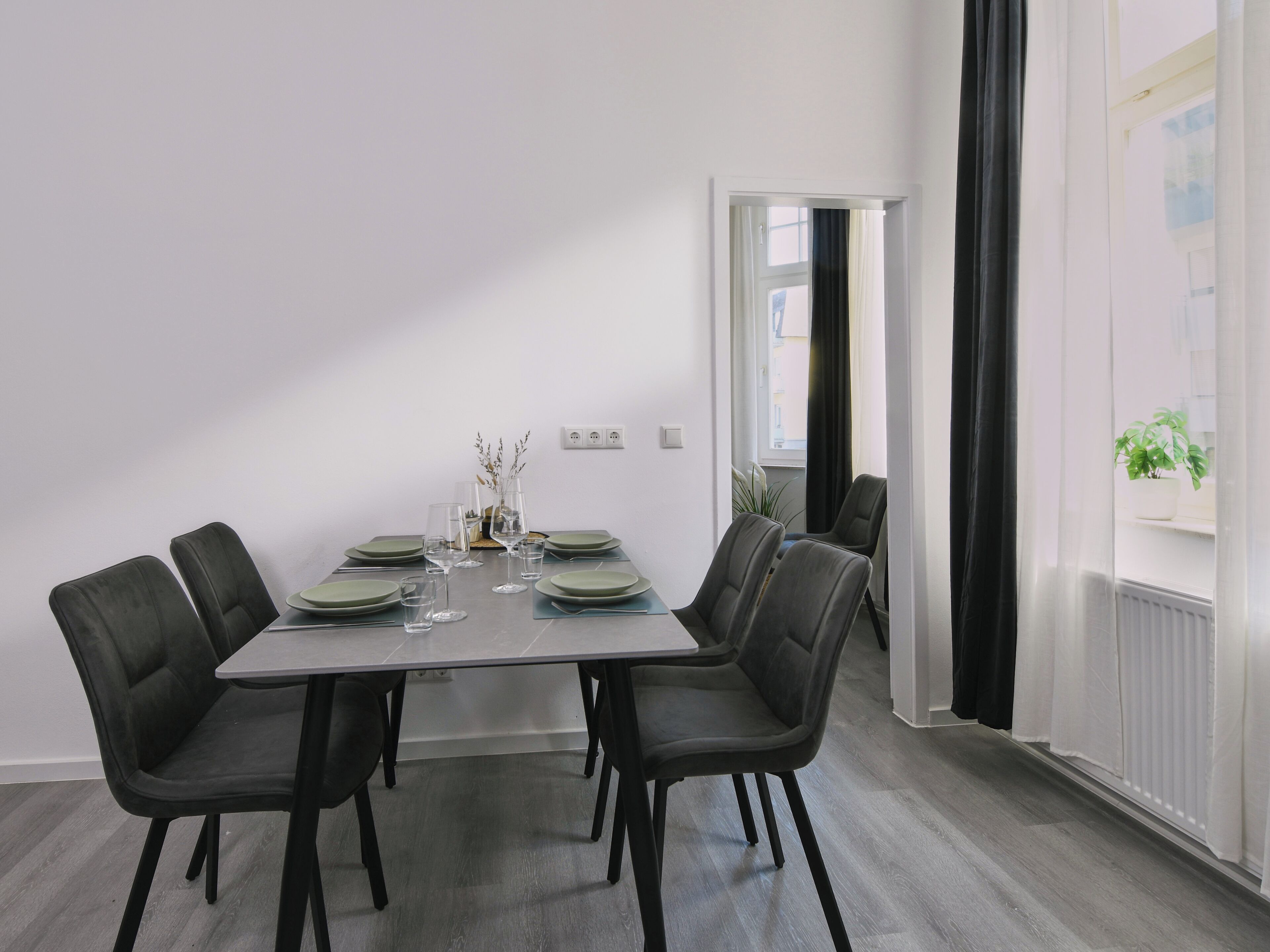 A dining area with a rectangular table, six chairs, and a window with curtains.
