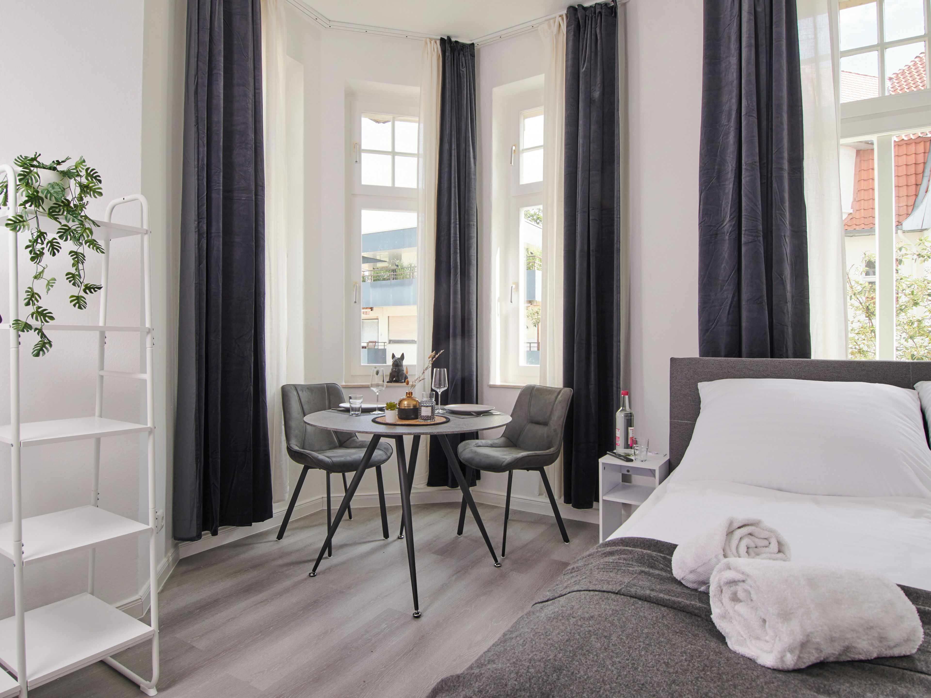 A hotel room with a bed, a round table with chairs, a small side table, and a plant.