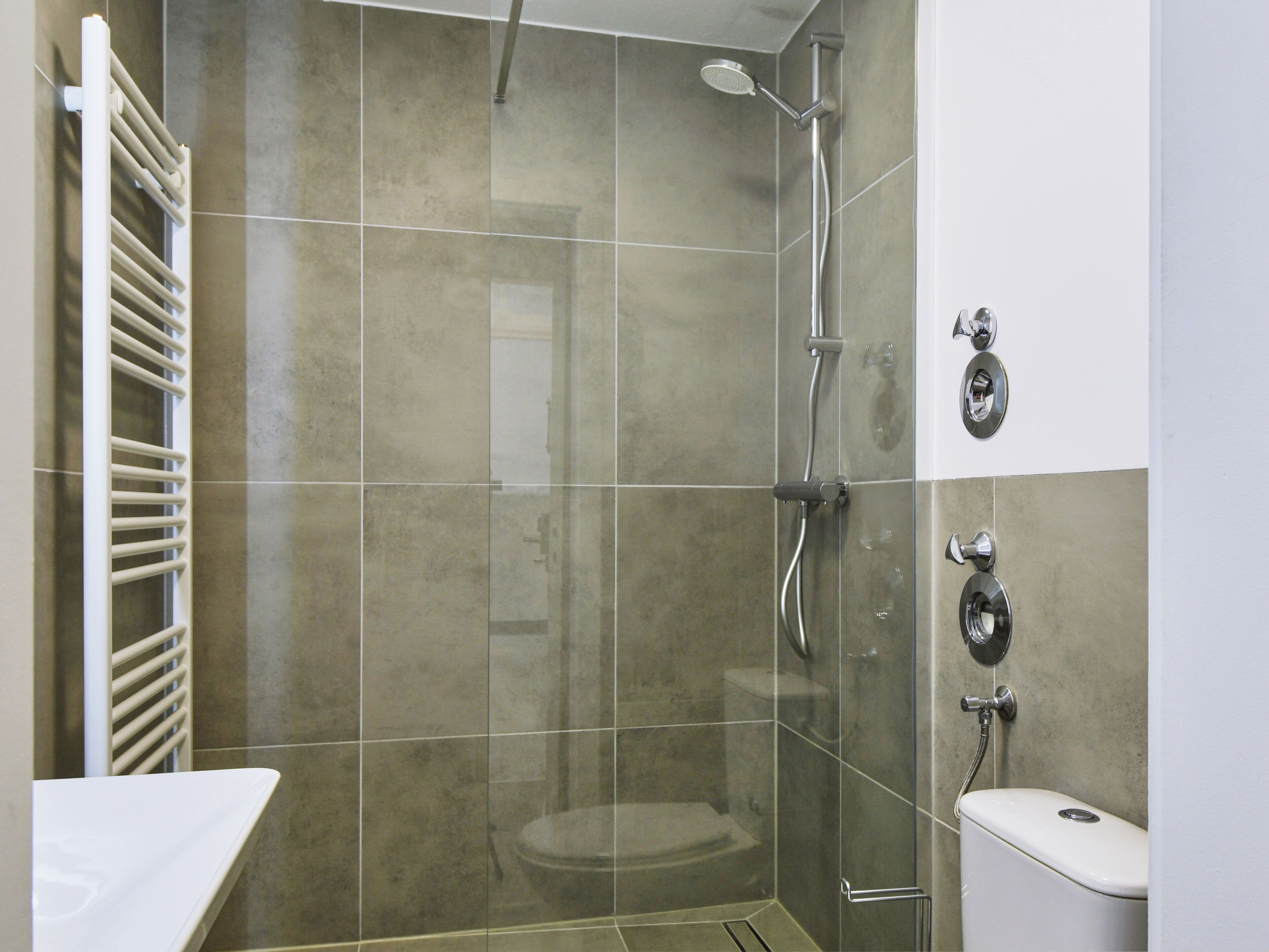 Een moderne badkamer met een douchecabine van glas, een wit toilet en een handdoekhouder.