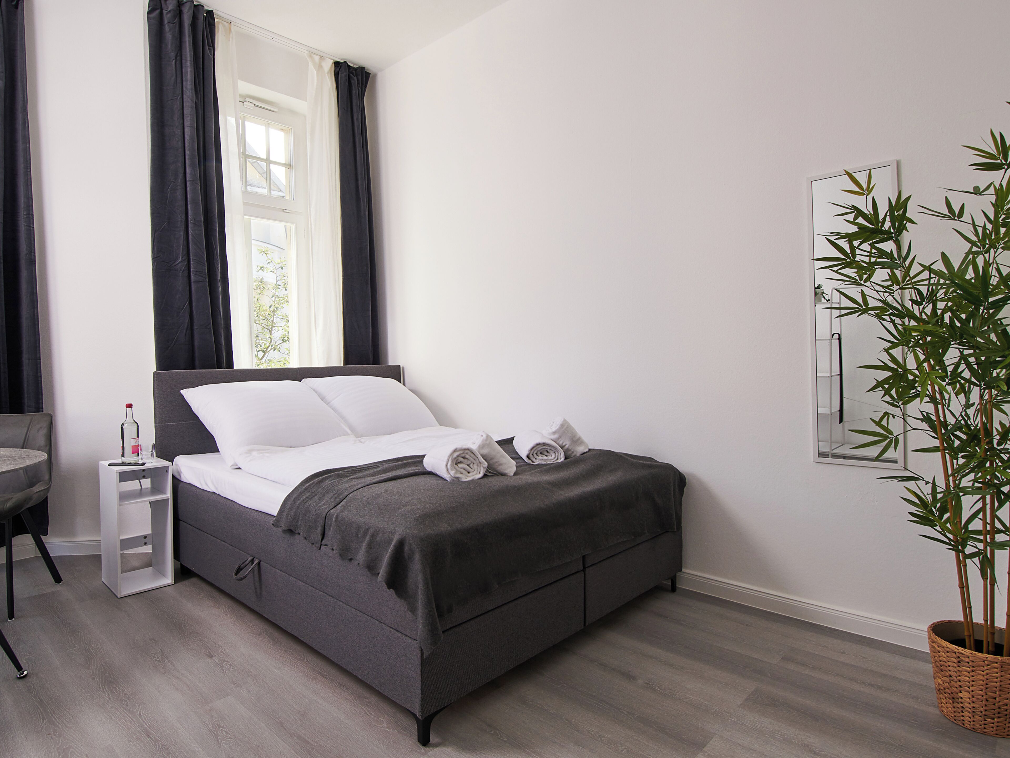 A modern bedroom with a bed, a nightstand, a chair, and a potted plant.