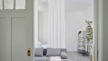 Ein modernes Wohnzimmer mit einem grauen Sofa, einem kleinen runden Tisch mit einer Fernbedienung und einem weißen Vorhang.